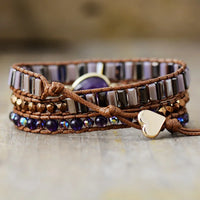 Multistrand bracelet with purple beads and heart charm button clasp, displayed  on a wooden surface