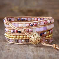 Multistrand beaded bracelet with pink beads and a gold button clasp charm on a wooden surface