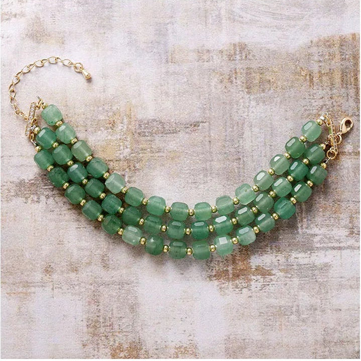 3-strand Green Aventurine beaded bracelet with gold accents displayed flat on a textured surface.