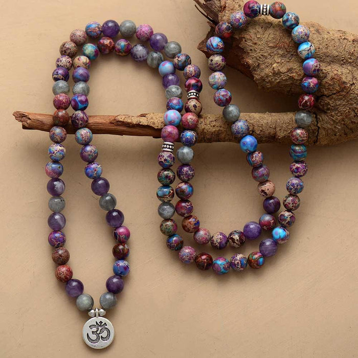 A stretchy bracelet with multicolored beads in various shades of purple, gray, and blue, featuring a silver-colored pendant with a symbol on it. ALLORA JADE