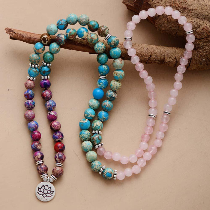 A stretchy Mala bracelet with a mix of blue, purple, and pink beads, featuring a silver pendant shaped like a lotus flower. ALLORA JADE