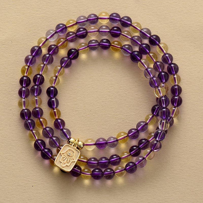 A stretchy Mala bracelet made of amethyst and citrine beads with a Hamsa hand charm. ALLORA JADE