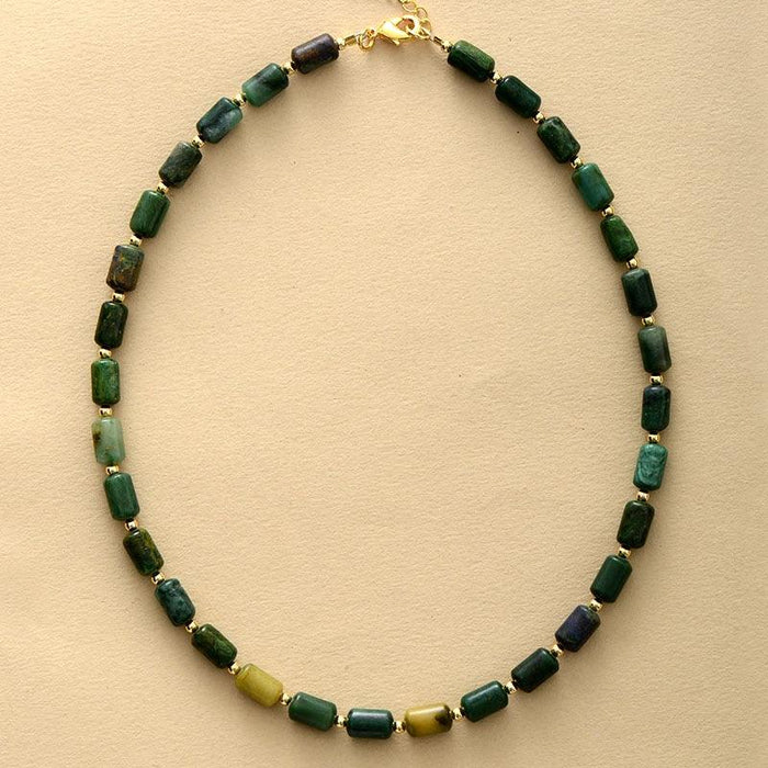 A green jade choker necklace with gold-colored beads and an extension chain, displayed on a wooden surface. ALLORA JADE